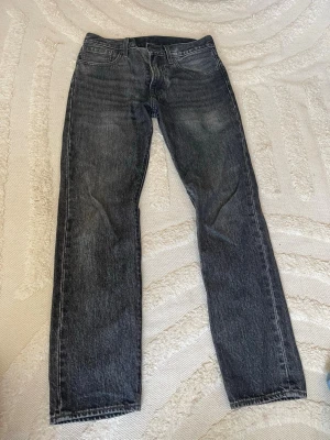 Svarta raka jeans från Levi's - Säljer ett par svarta raka jeans från Levi's med klassisk femficksdesign och läderpatch bak i midjan. Jeansen har en tvättad look och raka ben, perfekta för en avslappnad stil. Tillverkade i slitstarkt denimtyg.