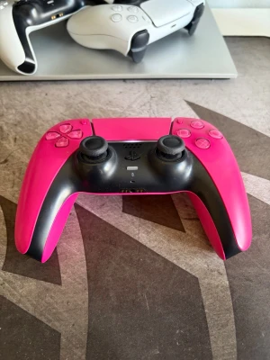 Rosa och svart PS5 DualSense handkontroll - Säljer en snygg rosa och svart PlayStation 5 DualSense handkontroll från Sony. Handkontrollen har en modern design med två analoga spakar, touchpad och klassiska PlayStation-knappar. Perfekt för gaming och passar till PS5.