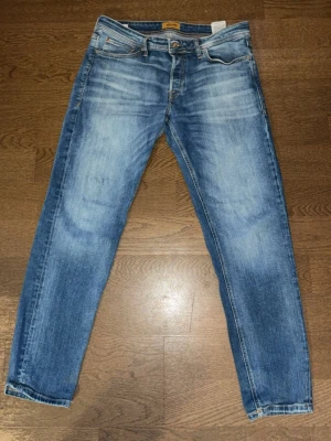 Mycket fina blåa jeans från jack&jones - Säljer ett par blå Jeans med klassisk femficksdesign och snygga detaljer på framsidan och baksidan. Jeansen har en skön passform och är tillverkade i bomull med detaljer i läder på bakfickan. Modellen på byxorna är tapered Mike.