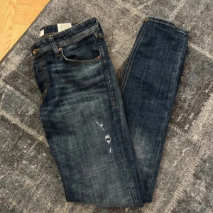 Jack & Jones - Säljer ett par Slim Glenn jeans i mörkblå tvätt med lätt slitna detaljer och klassisk femficksdesign. Jeansen har smal passform och normal midja. Perfekta för dig som gillar en stilren och modern look.