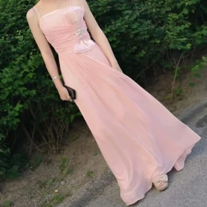 Ljusrosa långklänning med rosettdetalj - Säljer en jättefin ljusrosa långklänning med rosett framtill. Enda defekten är att den är lite smutsig nertill men ganska säker på att det försvinner i tvätt/kemtvätt! Storlek xxs-xs, använd 1 gång! Perfekt till balen och kan gå ner i pris