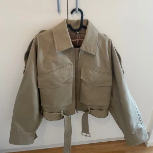 & another stories - Beige trenchcoat jacka med stora fickor  - Säljer en beige jacka med stora fickor framtill, dragkedja och bälte i midjan. HELT OANVÄND. Säljes pga av för stor på mig. 