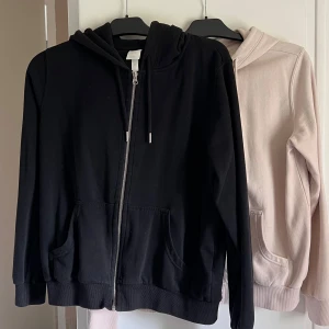 Ljusrosa och svart hoodie med dragkedja. Huvtröja med blixtlås - Säljer en ljusrosa (svårt att få rätt färg på bild) och en svart hoodie med dragkedja och huva. Tröjan har två fickor framtill och justerbara snören i huvan. Perfekt för en avslappnad stil och passar året runt. Använd fåtal gånger, dock har den rosa fått två små fläckar (knappt synbara på) men kan nog lätt tas bort med hjälp av solen eller fläckborttagning (jag har ej behandlat). M men passar S