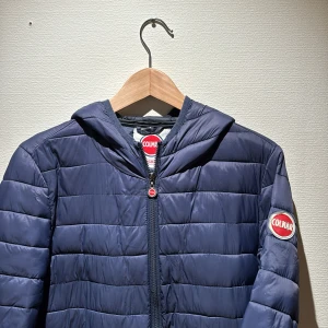 Blå pufferjacka från Colmar - Mörkblå pufferjacka från Colmar med huva och dragkedja framtill. Jackan är storlek medium men skulle säga att den funkar bra på small också, nypris på denna skönhet är 5000:- inget og tillkommer endast jacka.