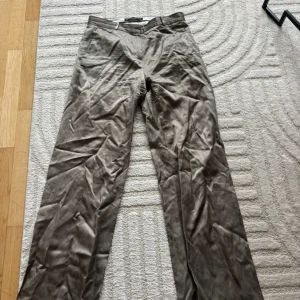 Beige kostymbyxor från Zara Basic - Snygga beige kostymbyxor från Zara Basic med klassisk passform och diskreta fickor. Perfekta för en stilren look och passar till många olika outfits. Byxorna har hällor för bälte och stängs med dragkedja och knapp.