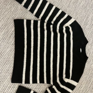 Svart och vit randig stickad tröja från H&M - Säljer en svart och vit stickad tröja från H&M med klassiskt randigt mönster. Tröjan har lång ärm och rund halsringning.