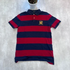 Randig pikétröja från Polo Ralph Lauren - Ralph Lauren Piké – Sportig & Stilren Säljer en klassisk pikétröja från Polo Ralph Lauren i storlek M. Breda röda och marinblå ränder, korta ärmar, krage med knappar och broderad gul logga på bröstet – en tidlös favorit!  🧵 Skick: Nyskick 💸 Pris: Endast 99 kr! 🛍️ Originalpris: 1000–1300 kr  Perfekt för dig som vill ha en sportig och stilren look i sommar. 📩 Skicka DM om du vill köpa!