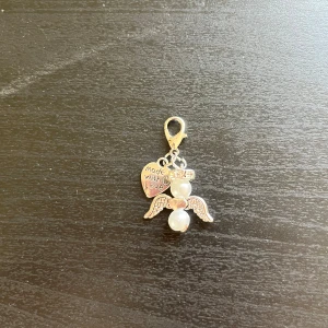 Ängelberlock med pärlor och hjärta 💕  - Söt berlock i form av en ängel med vita pärlor och silverfärgade vingar. Fästet är en karbinhake och det hänger även ett hjärta med texten 'made with love'. Perfekt som accessoar till väska eller smycke. 💕