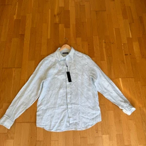 Ljusblå linneskjorta från J.Lindeberg - Säljer denna Snygg ljusblå skjorta i linne från J.Lindeberg. Skjortan är helt NY perfek för en stilren och avslappnad look. Skjortan har en lätt och luftig känsla tack vare linnematerialet. ny pris 1000kr+ size L