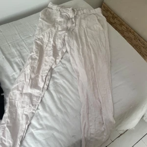 Vita linnebyxor  - Säljer ett par vita linnebyxor med dragsko i midjan. Byxorna har en avslappnad passform och är perfekta för varma dagar. De har bälteshällor och är tillverkade i ett lätt och luftigt material.