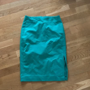 Grön pennkjol från InWear - Säljer en grön pennkjol från InWear med slits på sidan och dragkedja bak. Kjolen har en stilren och klassisk form som passar perfekt till många olika looks. Materialet känns mjukt och har en lätt glans.
