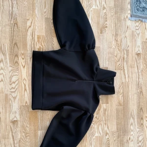 Svart tröja med puffärmar - Säljer en svart tröja med markerade puffärmar och hög krage. Tröjan har en dragkedja framtill och en stilren, minimalistisk design. Perfekt för dig som vill ha en trendig och snygg look.