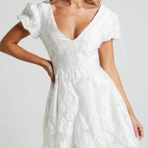 Vit jacquardklänning med puffärm - Superfin vit kortklänning i jacquard med puffiga ärmar och v-ringning. Klänningen har ett subtilt blommönster i tyget och öppen rygg. Perfekt för sommarens tillfällen och studentfirande. Klänning var däremot sönder vid dragkedjan när jag fick hem den, därav priset. Men det kan enkelt lagas💞