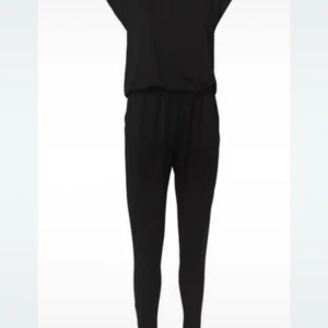 Svart byxdress  från By Malene Birger - Säljer en svart byxdress från By Malene Birger. Byxdressen har en lös passform med resår i midjan och korta ärmar. Perfekt för dig som gillar stilren och minimalistisk design.
