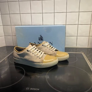 Beige sneakers från Lanvin - Snygga beige sneakers från Lanvin med rund tå och snörning. Skorna har en stilren design med en glansig tåhätta som ger en extra touch. Perfekta för en avslappnad men ändå elegant look.