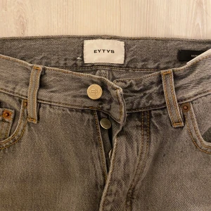 Grå jeansbyxor från Eytys - Säljer ett par raka grå jeans från Eytys med klassisk femficksdesign och synliga kontrastsömmar. Byxorna har hög midja och stängs med knapp och dragkedja. Perfekta för dig som gillar en stilren och enkel look.
