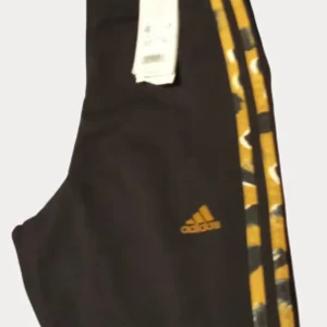 Svarta Adidas träningstights med gula detaljer - Säljer ett par svarta träningstights från Adidas med gula ränder och logga på benet. Snygg design med klassiska Adidas-detaljer längs sidorna. Perfekta för gymmet eller löprundan.