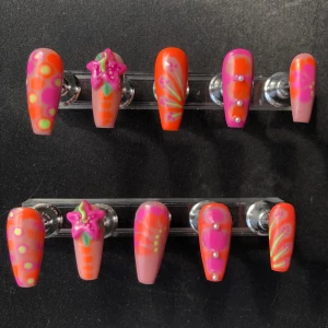 Färgglada lösnaglar med blommönster och pärlor - Säljer ett set handgjorda lösnaglar i orange, rosa och grönt med handmålade blommor, prickar och linjer. Vissa naglar har 3D-blommor och små pärlor som dekoration. Perfekt för dig som vill ha en unik och färgstark nageldesign.