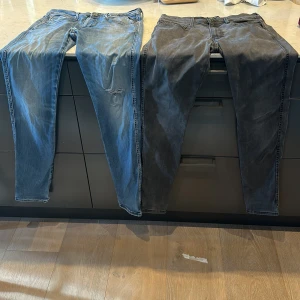 Replay jeans i blått och svart - Två par Replay jeans säljes, ett par i klassiskt blått med slitningar och snygga bakfickor med broderad detalj, och ett par i mörkare svart tvätt. Båda har smal passform och är tillverkade i mjukt jeanstyg. Perfekta för dig som gillar stilrena och bekväma jeans.