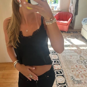 Svart linnetopp med spetskant - Säljer en svart linnetopp med tunna axelband och snygg spetskant längs urringningen. Toppen är croppad och har en enkel, stilren look som passar perfekt till jeans eller kjol. Materialet känns mjukt och lätt mot huden.