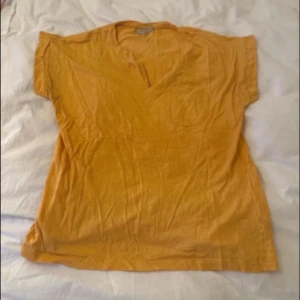 Gul v-ringad blus i bomull - Snygg gul blus med v-ringning och korta ärmar. Tillverkad i mjuk bomull, perfekt för en avslappnad och trendig look. Enkel design som är lätt att matcha med jeans eller kjol.