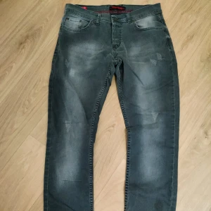 Replay jeans i mörkgrå tvätt - Säljer ett par snygga Replay jeans i mörkgrå tvätt med slitna detaljer och klassisk femficksmodell. Jeansen har normal passform och raka ben, perfekt för en avslappnad stil. Tidlös design med Replay-logga på insidan av linningen.