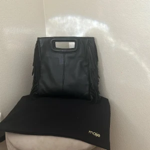 Svart fransad handväska från Maje - Säljer min fina Maje väska. Använd fåtal gånger. Kommer även med bandet. Original pris 3 299 kr. 