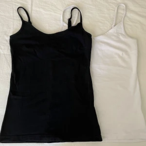 Svart och vit linnetopp med smala band - Två stilrena linnetoppar i svart och vitt med smala axelband och enkel, rak passform. Perfekta att matcha med jeans eller kjol. Mjukt bomullsmaterial som känns skönt mot huden och passar till alla säsonger.