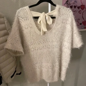 Beige stickad tröja med knytband - Säljer en söt beige stickad tröja med korta ärmar och ett dekorativt knytband i nacken. Perfekt för en mysig och stilren look och passar till allt