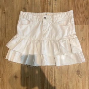 Vit volangkjol från Gina Tricot - Supersöt vit kortkjol från Gina Tricot med två lager volanger och rå kant nedtill. Kjolen har klassiska jeansdetaljer som fickor och knapp och är aldrig använd.💞💞