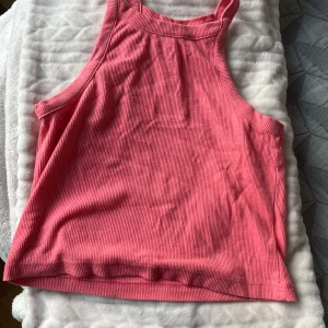 Rosa ribbad linnetopp från Divided - Säljer en rosa ribbad linnetopp från Divided (H&M). Toppen har en högre halsringning och är ärmlös med breda axelband. Perfekt för varma dagar eller att styla lager på lager. Mjuk och stretchig bomullskvalitet.