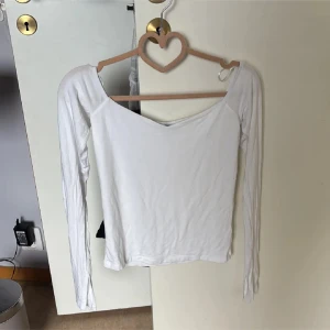 Vit långärmad topp från Gina Tricot - Säljer en vit långärmad topp från Gina Tricot i storlek M. Modellen har en snygg v-ringad hals och offshoulder-design som ger en cool vibe. Materialet är mjukt och stretchigt, troligen bomull. Perfekt att styla med jeans eller kjol för en fräsch look.