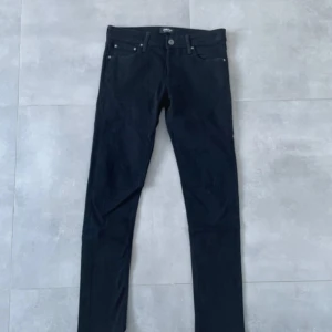 Svarta skinny jeans från Jack & Jones - Svarta jeans från Jack & Jones med klassisk femficksdesign och smal passform. Jeansen har normal midja och raka ben med skinny fit. Tillverkade i stretchig bomullsblandning för extra komfort. Perfekta för en clean och stilren look.