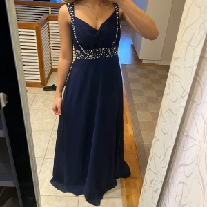 Mörkblå balklänning med strass -  mörkblå lång balklänning från Scala med vringad omlott topp och glittriga strassdetaljer längs axelband och midja. har breda axelband, Jätte fin och perfekt till balen!! Skulle säga att den satt som en S. Använd 1gång, bilderna är från hon jag köpte den ifrån. 