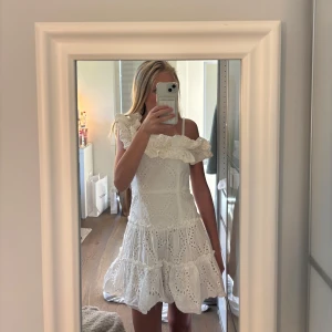 Vit volangklänning från Zara - Superfin vit kort klänning från Zara med volanger och broderade detaljer. Klänningen har axelbandslös look med smala axelband, omlottvolang upptill och flera lager i kjolen. Perfekt för sommarens alla tillfällen!