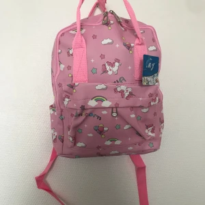 Barn ryggsäck med enhörningsmönster  - Supergullig rosa ryggsäck med enhörningar, regnbågar, stjärnor och moln. Väskan har justerbara axelband, bärhandtag och en praktisk framficka med dragkedja. Perfekt för dig som älskar färgglada och lekfulla accessoarer.