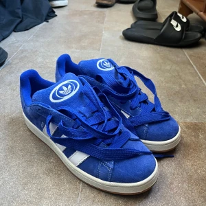 Blå adidas Campus sneakers mocka - Snygga blå adidas Campus sneakers i mocka med klassiska vita ränder på sidorna och stor adidas-logga på plösen. Skorna har rund tå, platt sula och snörning. Helt nya, endast använda två gånger.