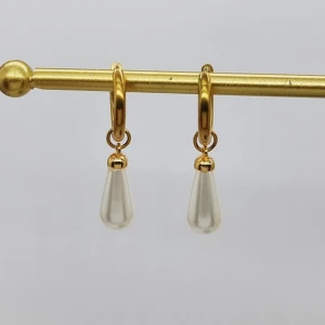 Guldiga örhängen med pärldroppar - Snygga örhängen med rund guldfärgad ring och hängande droppformad pärla i vitt. Perfekt för dig som gillar stilrena och eleganta smycken med en modern twist. De har en klassisk look med en liten lyxig känsla tack vare pärldetaljen.
