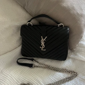 Svart YSL handväska  - Säljer en svart quiltad handväska, ej äkta. Väskan har kedjerem i silver, top handtag och dragkedja inuti.  Perfekt storlek för mobil och essentials.