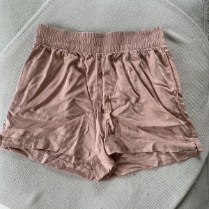 Rosa shorts från Kay/Day i S - Mjuka och sköna shorts från Kay/Day i en ljusrosa nyans. De har elastisk midja och är tillverkade i ett tunt, svalt material som känns riktigt bekvämt. Perfekta för varma sommardagar eller att chilla hemma i. Enkel och stilren design utan mönster eller extra detaljer.