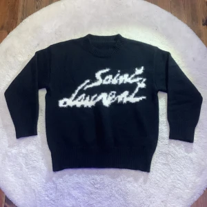 Svart stickad Saint Laurent tröja - Svart stickad tröja i strl S från Saint Laurent med vit, fluffig logotyp framtill. Rund hals och långa ärmar med ribbade muddar. Tröjan har en loose passform och är perfekt för dig som gillar exklusiva märken och vill sticka ut med en cool design. Skriv vid fler frågor elr intrsse👍
