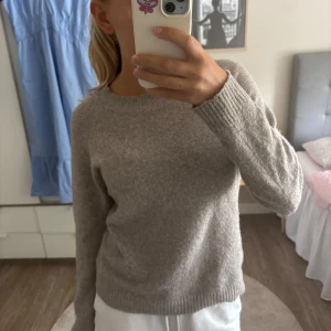 Beige stickad tröja från Vero Moda - Mysig beige stickad tröja från Vero Moda med rund hals och långa ärmar. Tröjan har en enkel och clean design med ribbade muddar vid hals, ärmslut och nederkant. Perfekt för att hålla sig varm under kyliga dagar.