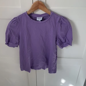 Lila topp med puffärm från Vero Moda - Superfin lila topp från Aware by Vero Moda i bomull. Modellen har korta puffärmar. Den är i storlek XS och säljs då den inte används.