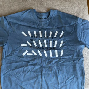 Blå Maison Margiela t-shirt med print - Snygg blå t-shirt från Maison Margiela med ikoniskt grafiskt print och siffror framtill. Klassisk rund hals och korta ärmar. Tillverkad i mjuk bomull som känns skön mot huden. Perfekt för dig som gillar statement-plagg och unik design. | Priset är INTE hugget i sten! 🙅‍♂️❌