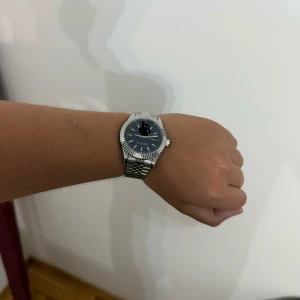 Blå-silver klocka med länkarmband - Stilren klocka från Oyster Perpetual med blå urtavla och datumvisning. Boetten och det klassiska länkarmbandet är i silverfärgat metall. Urtavlan har tydliga index och vriden bezel som ger en cool look. Perfekt accessoar för dig som gillar tidlös design.