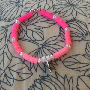 Handgjort rosa pärlarmband med hamsa-berlock - Unikt armband med rosa och ljusrosa platta pärlor, vita pärlor och en snygg hamsa-hand i metall som berlock. Armbandet har ett guldfärgat lås och är ca 19 cm långt. Perfekt för dig som gillar färgglada accessoarer med coola detaljer.