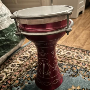 Ingen bok synlig - Bilderna visar en röd dekorerad darbuka, ett slagverksinstrument, och ingen bok. Perfekt för dig som vill skapa rytmer och musik med vänner eller på egen hand.