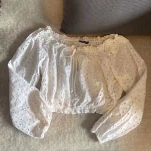 Vit broderad blus från Gina Tricot - Supersöt vit blus från Gina Tricot i storlek XS. Blusen är croppad med långa puffärmar, resår i midjan och vid ärmslut. Använd 1 gång.