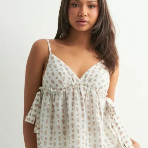 Vit blommig linnetopp med knytband - Supersöt vit linnetopp med tunna axelband och ljusbrunt blommönster. Toppen har v-ringning och knytband i sidorna 