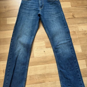 Blå jeans från Replay, rak modell - Säljer ett par klassiska blå jeans från Replay i rak passform. Jeansen har snygga slitningar framtill, fem fickor och tydliga sömmar på bakfickorna. Tillverkade i jeansmaterial med en cool tvättad look. Perfekta för dig som gillar en tidlös stil.